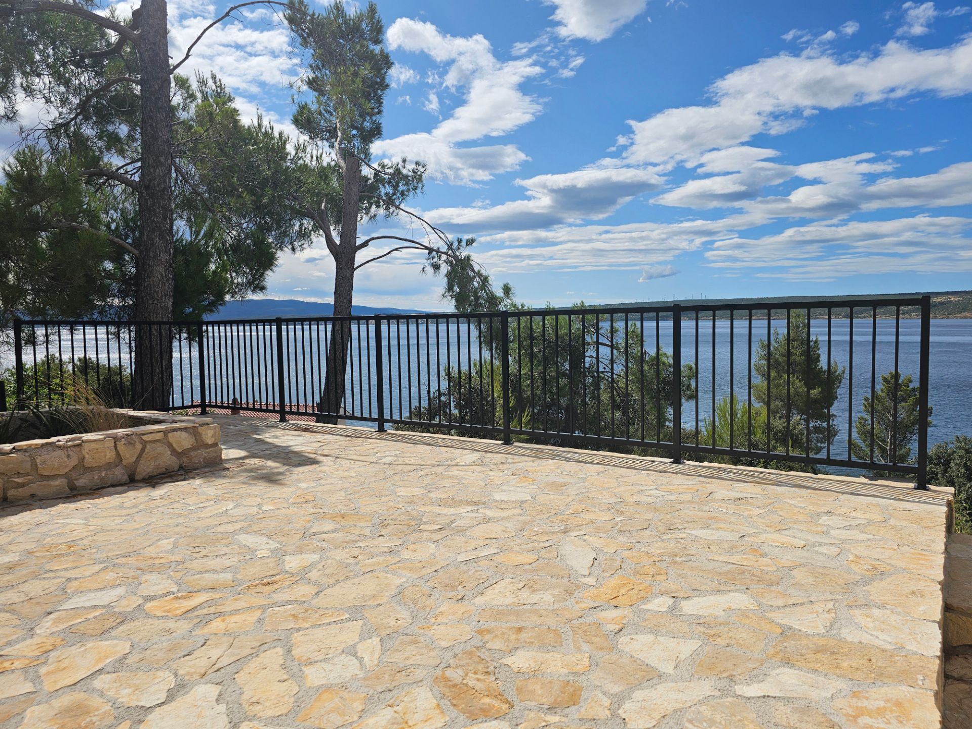 Edelstahl-Balkongeländer mit Seeblick Elegantes Edelstahl-Balkongeländer mit Rundstäben und Natursteinboden mit Seeblick